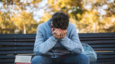 Teenager sits on a bench in the park and listen to music and learning for exame