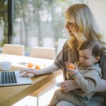 mom holding child and looking on computer.