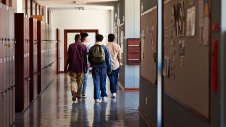 Full length rear view of male teenage students walking by lockers in corridor at high school